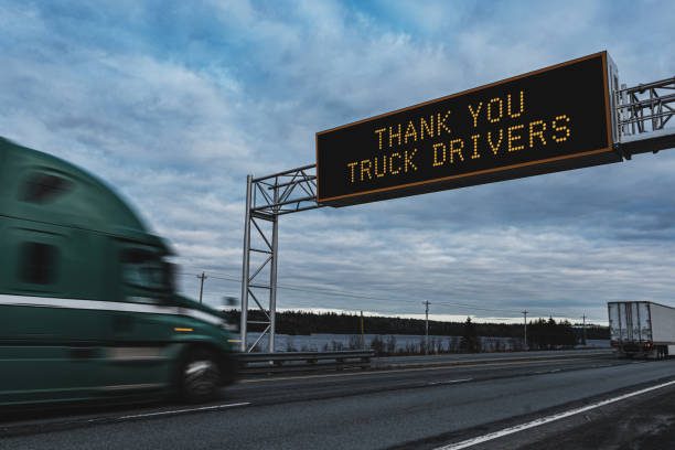 State of Emergency Obey Public Health Orders on an overhead highway sign during the Coronavirus pandemic, out of focus semi truck in foreground.