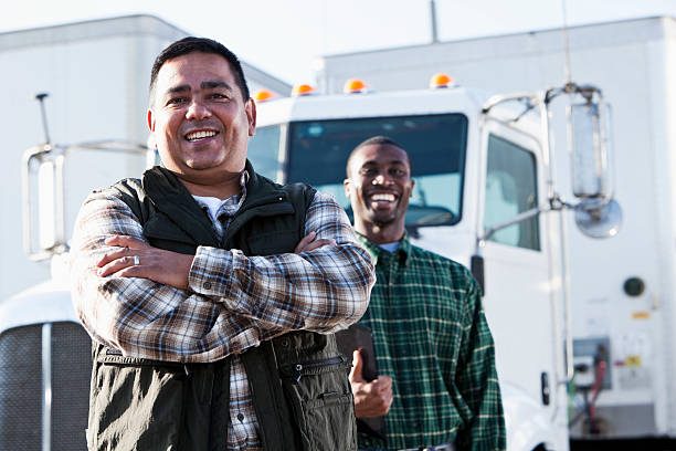 Hispanic and African American truck drivers standing in front of semi-truck.  Focus on Hispanic man (40s).